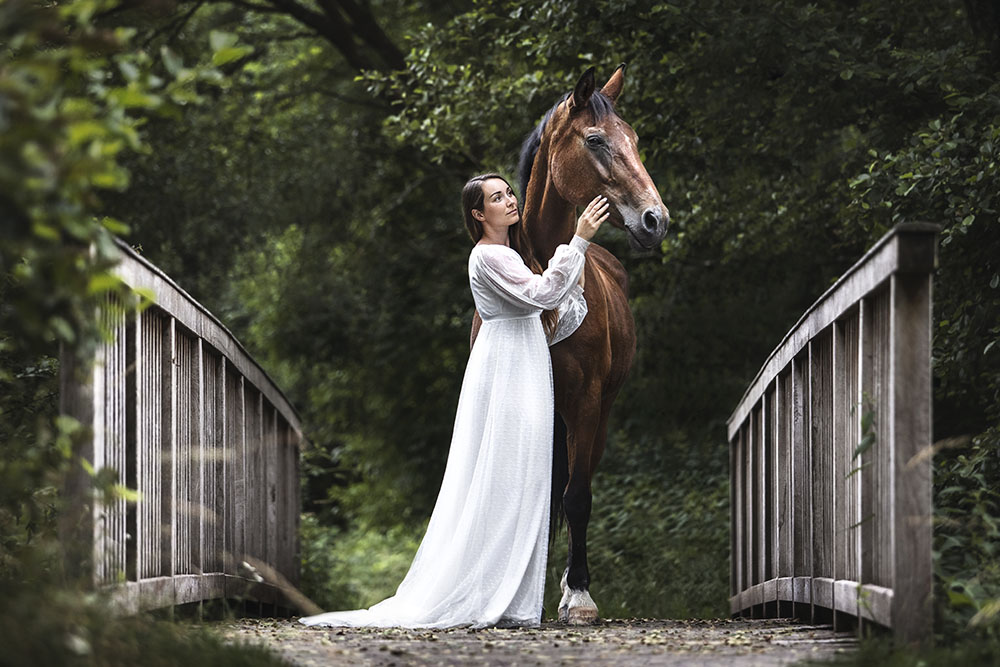 Fotografie von einem Pferd mit einer Frau auf einer Holzbrücke vor einem Wald bei einem Pferdeshooting in NRW im Sommer von Vivien Schust Photography
