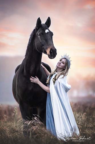 Magic Fotoshooting einer Göttin in einem blauen Kleid mit einem weißen Umhang und einer silbernen Krone mit ihrem Pferd im Sonnenuntergang bei einem Pferdeshooting in Köln von Vivien Schust Photography