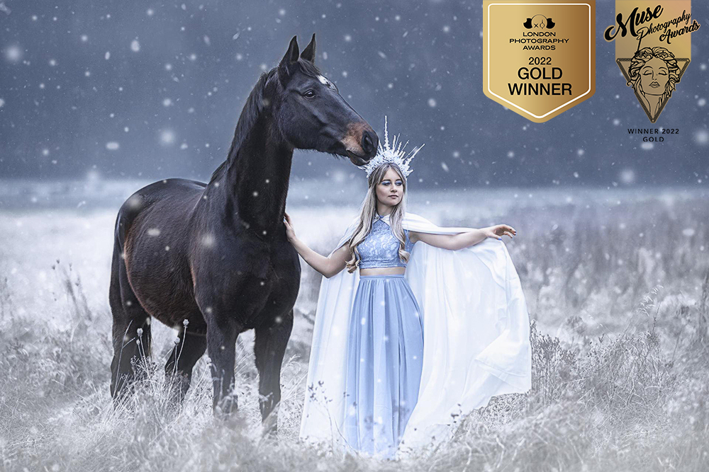 Dieses Bild zeigt eine Eiskönigin im hellblauen Kleid mit einem weißen Umhang und einer Krone mit ihrem Pferd im Schnee. Mit diesem Bild habe jeweils eine Gold Auszeichnung beim Muse Photography Awards 2022 und eine beim London Photography Awards 2022 gewonnen.