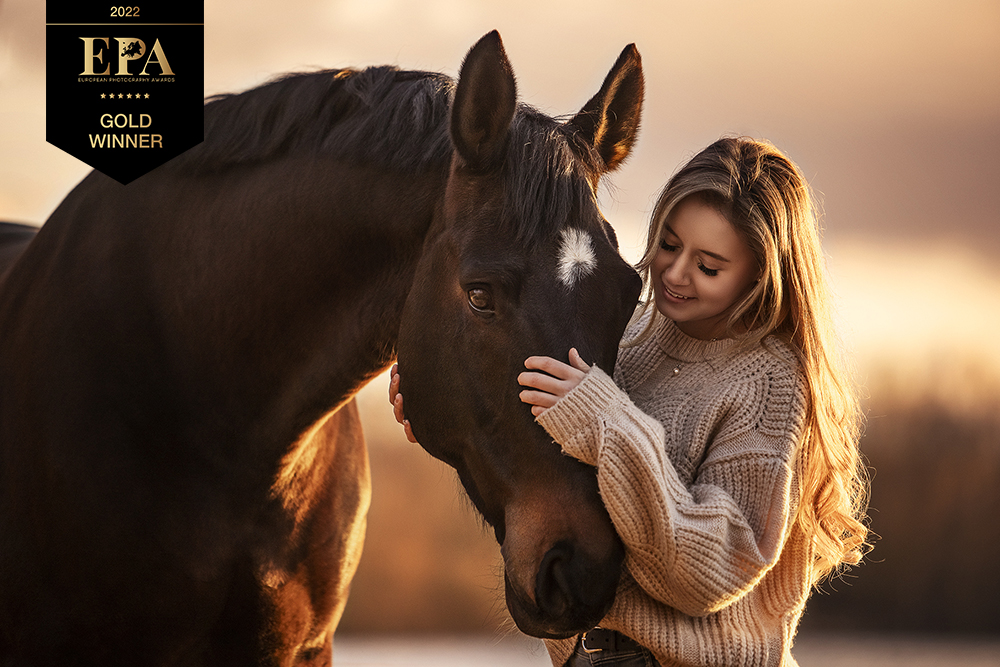 Dieses Bild zeigt eine Frau mit ihrem Pferd im Sonnenuntergang, welches beim European Photography Awards 2022 mehrfach mit dem Titel Gold Winner ausgezeichnet wurde