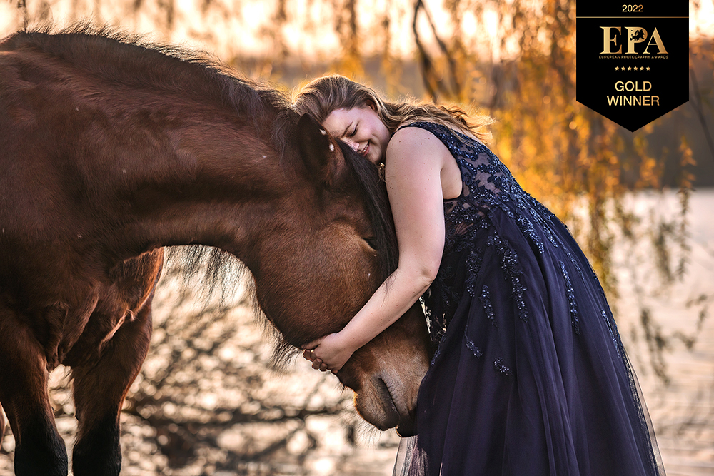 Dieses Bild zeigt eine Frau mit ihrem Pferd im Sonnenuntergang am See, welches beim European Photography Awards 2022 mehrfach mit dem Titel Gold Winner ausgezeichnet wurde